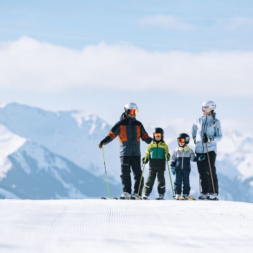 Zwei Erwachsene und zwei Kinder auf einer Skipiste in den Alpen
