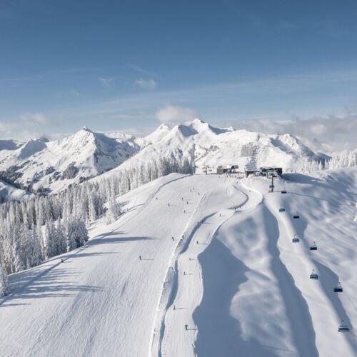 Skipiste und blauer Sessellift in einer tiefverschneiten Landschaft in den Alpen